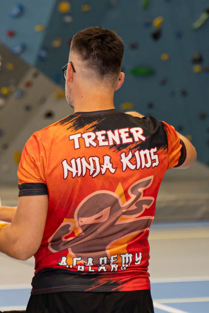 Rekrutacja trenerów 1 Trener Ninja Kids Academy stojący odwrócony do kamery. Posiada koszulkę trenera Ninja Kids Academy z logo