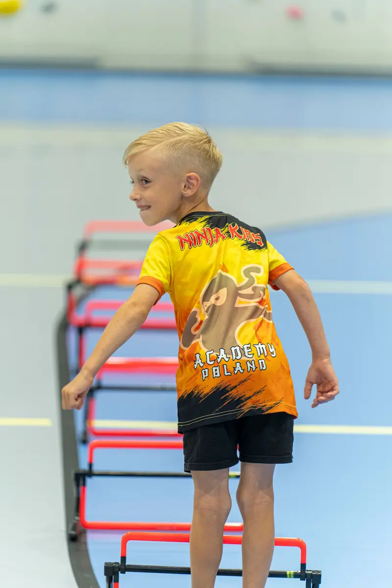 Rekrutacja trenerów 3 Mały chłopiec patrzy do tyłu w trakcie pokonywania przeszkód w Ninja Kids Academy